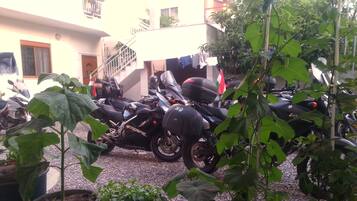 A parking area with multiple motorcycles, a building with a staircase, and potted plants.