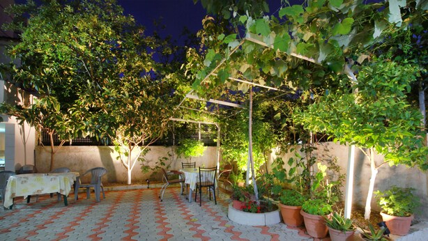 An outdoor patio area with a tiled floor, tables, chairs, and potted plants.