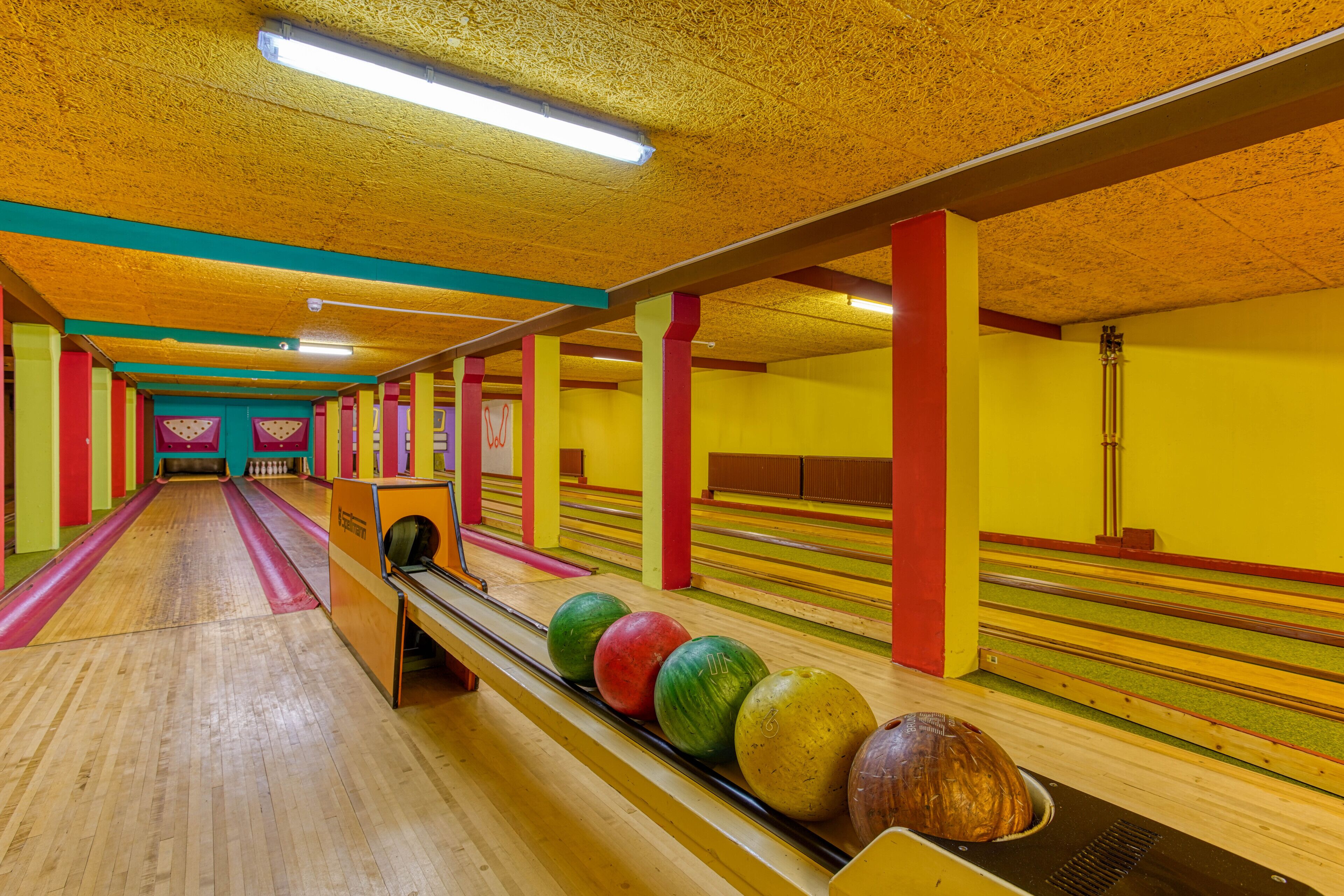 Une salle de bowling dotée de nombreuses pistes, de planchers en bois et de murs aux couleurs vives.