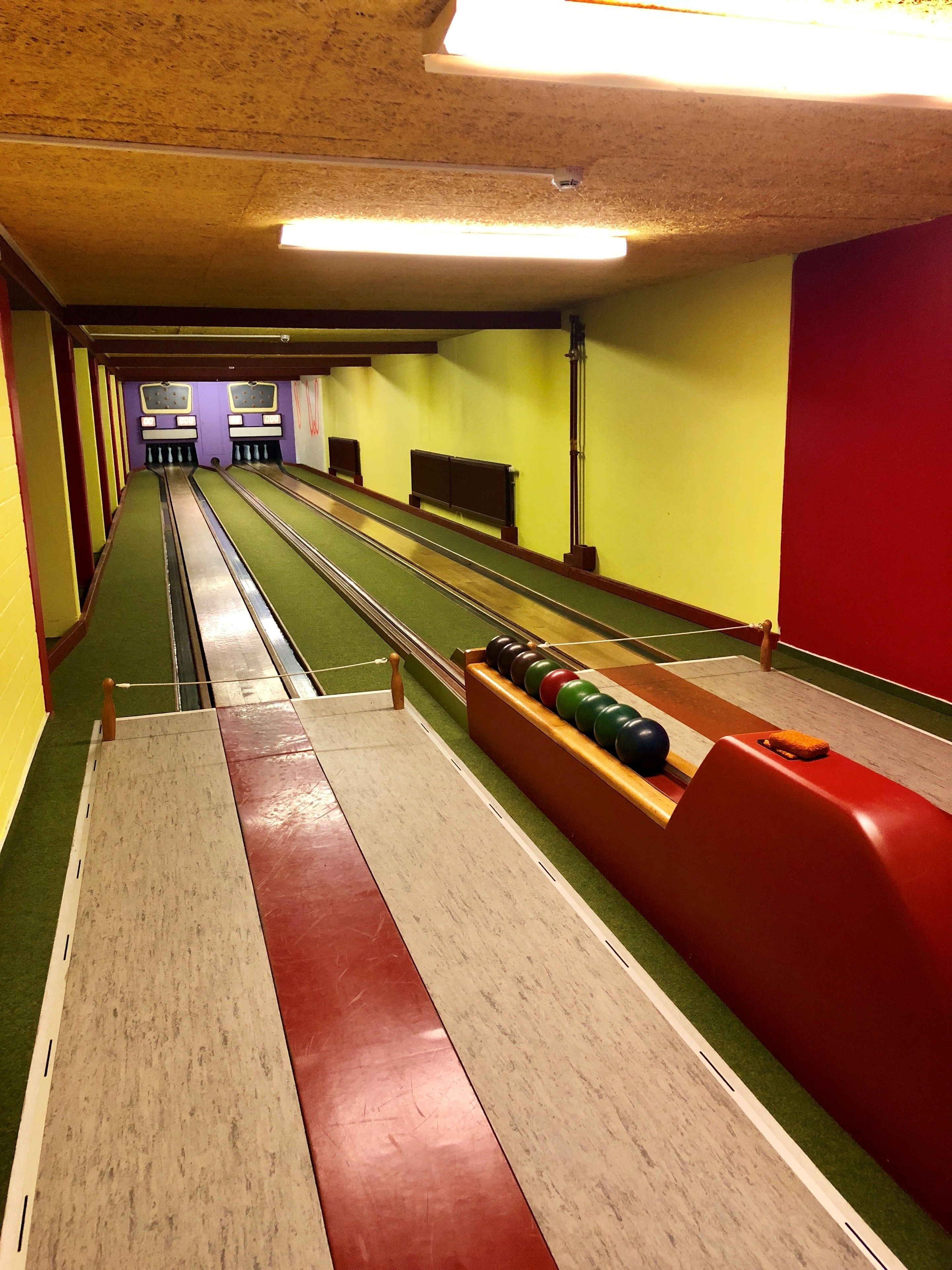 Bolera con múltiples pistas, suelo cubierto de moqueta verde y bolos de madera.
