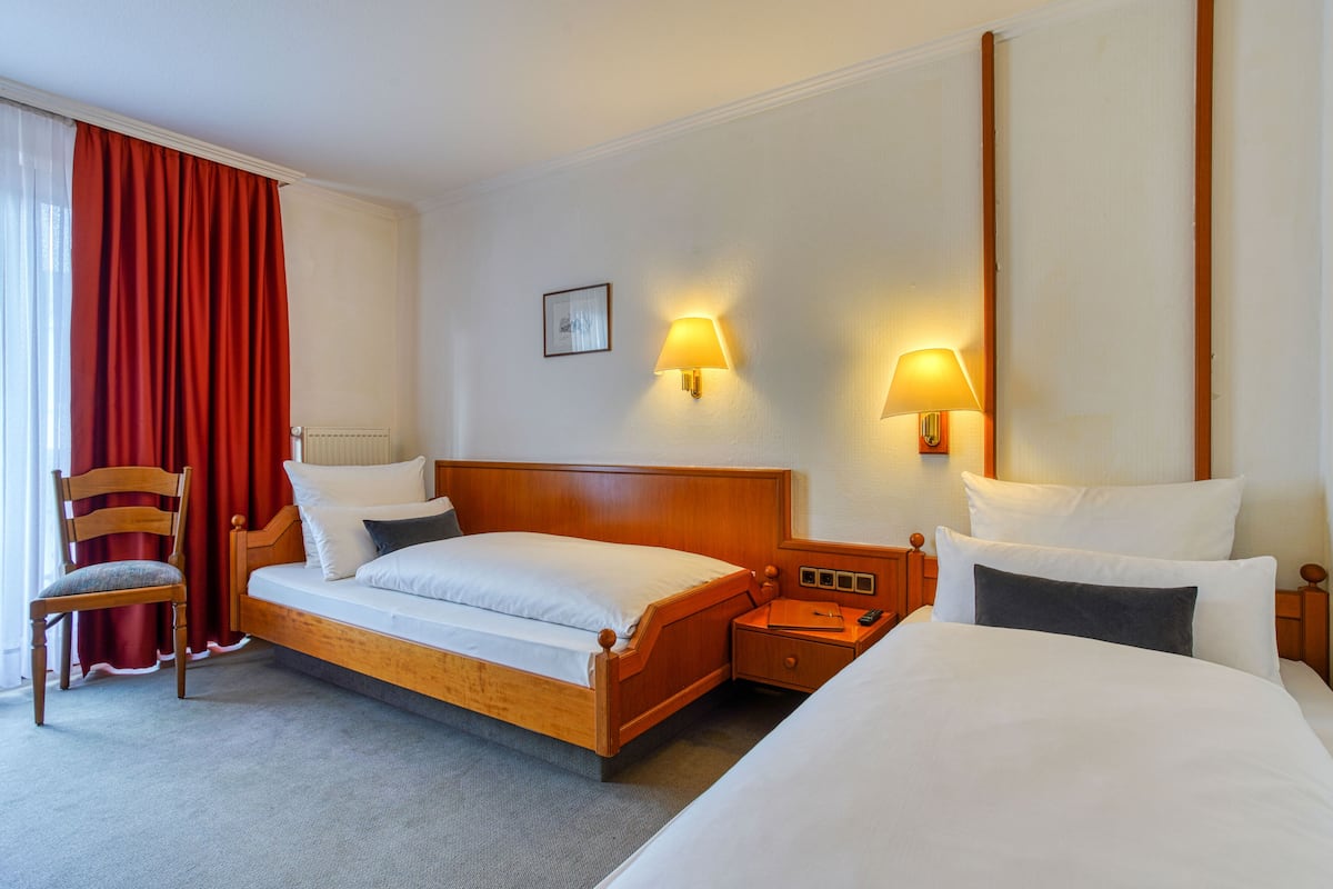 Ein Hotelzimmer mit einem hölzernen Bett, einem Sessel, zwei Nachttischen und zwei Wandleuchten.