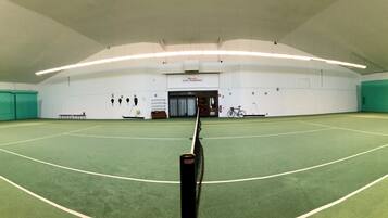 En indendørs tennisbane med et net i midten, omgivet af grønne vægge og hvide lofter.