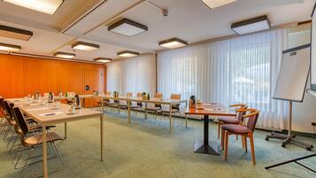 Une salle de conférence équipée de plusieurs tables et chaises, d’un tableau blanc et de grandes fenêtres avec des rideaux.