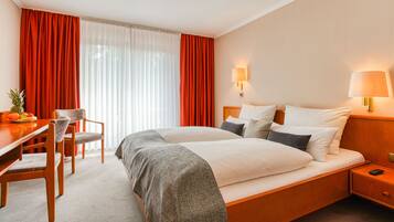 Una habitación de hotel con una cama grande, dos mesitas de noche, un escritorio con una silla y un frutero sobre el escritorio.
