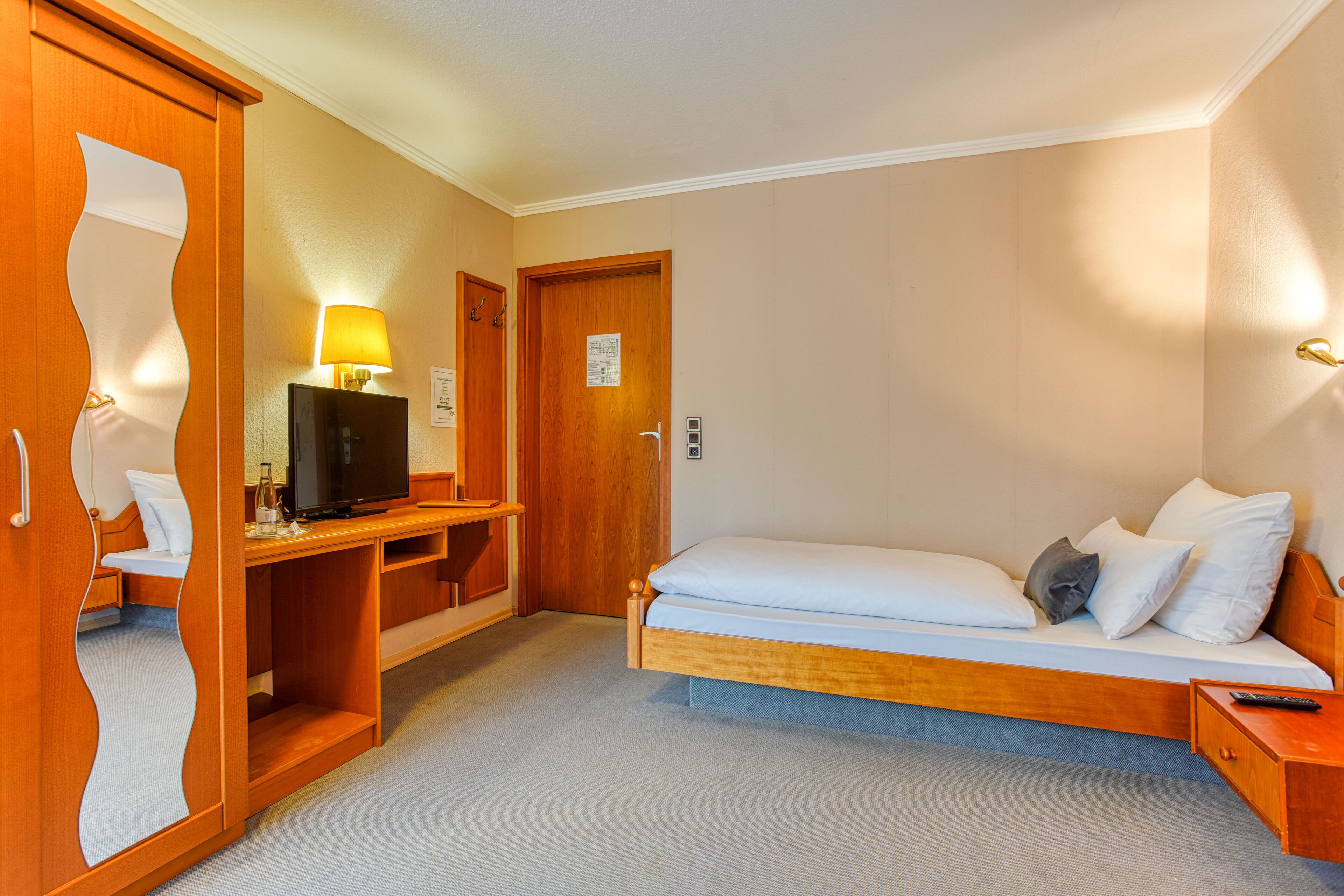 A compact hotel room with a bed, a desk with a lamp, a television, and a wardrobe.