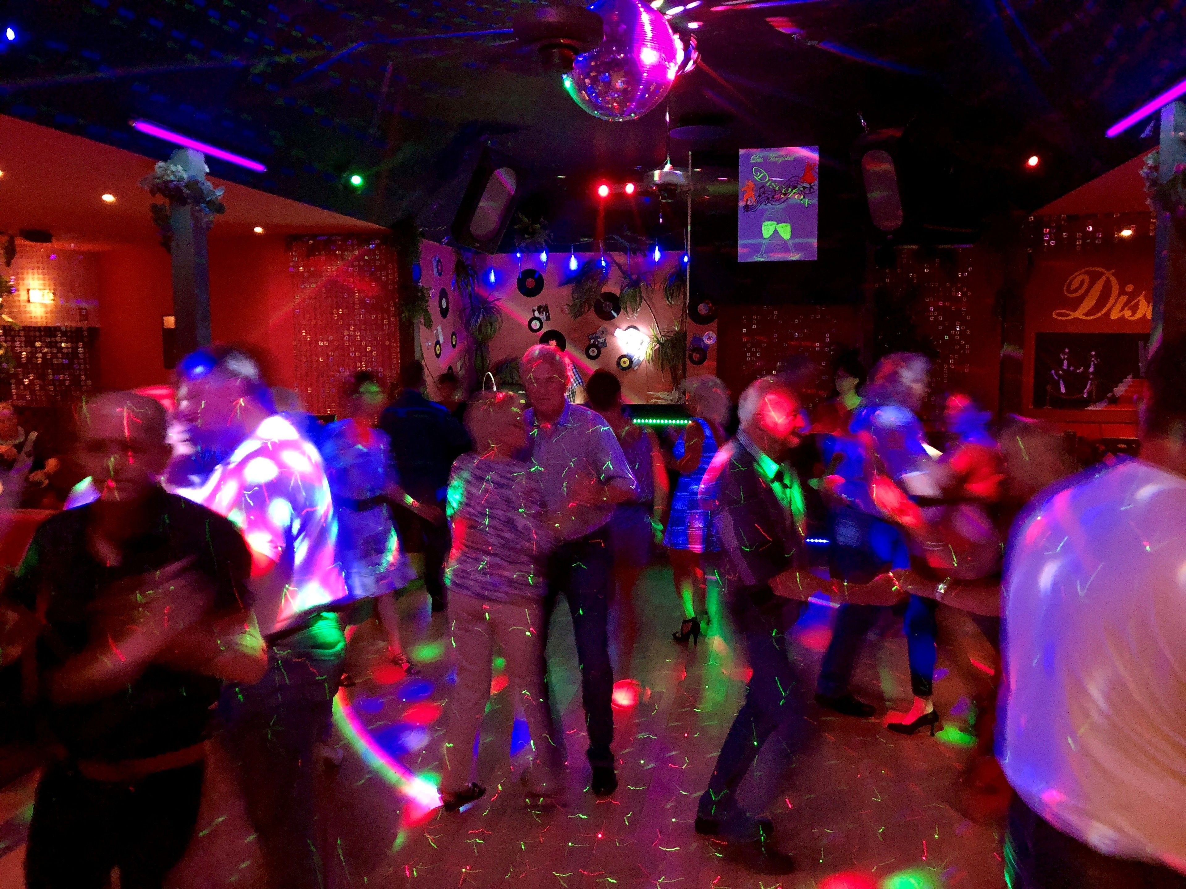 A crowded dance floor with people dancing, disco balls, and a DJ booth.