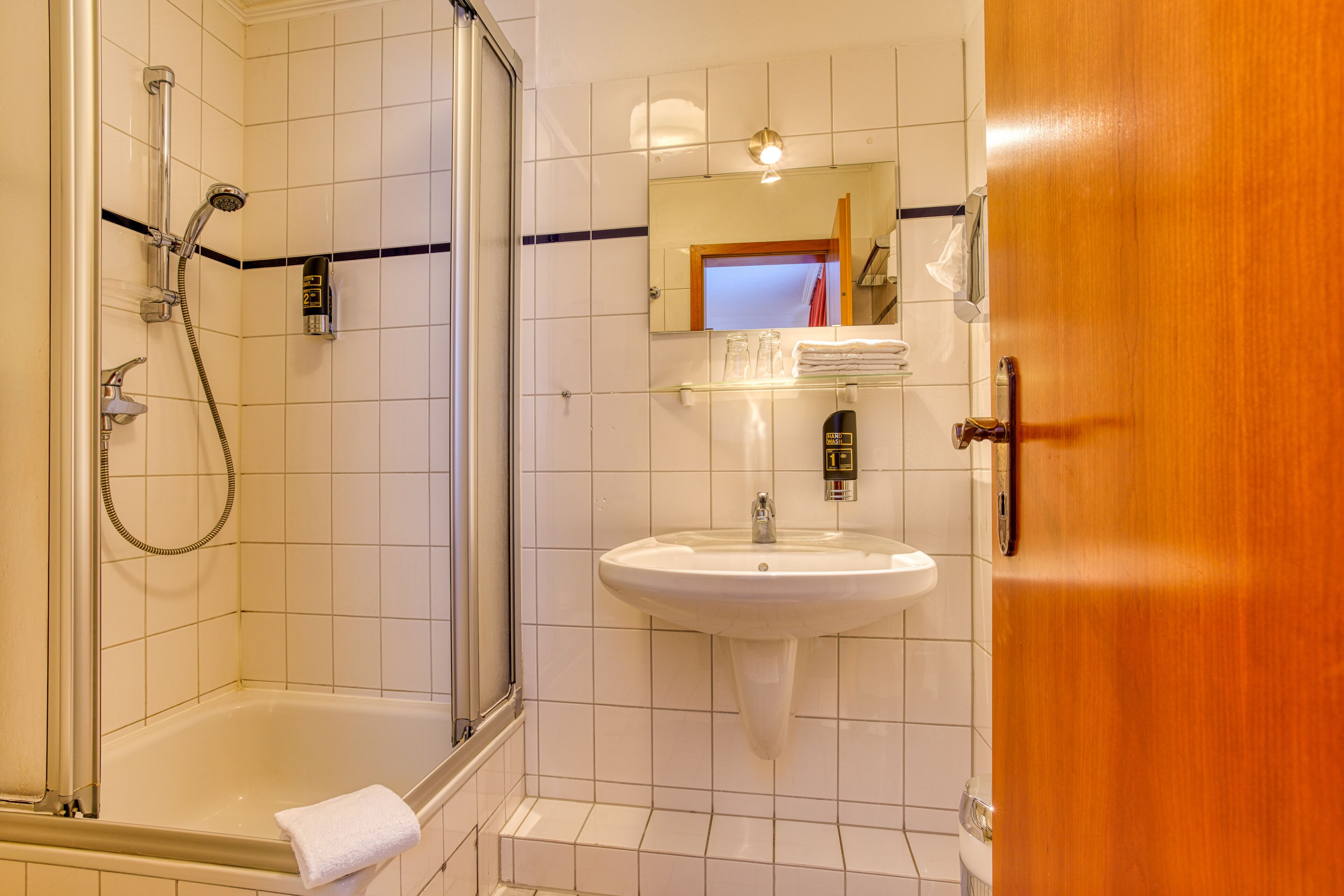 A bathroom with a glass-enclosed shower, a white sink, and a wooden door.