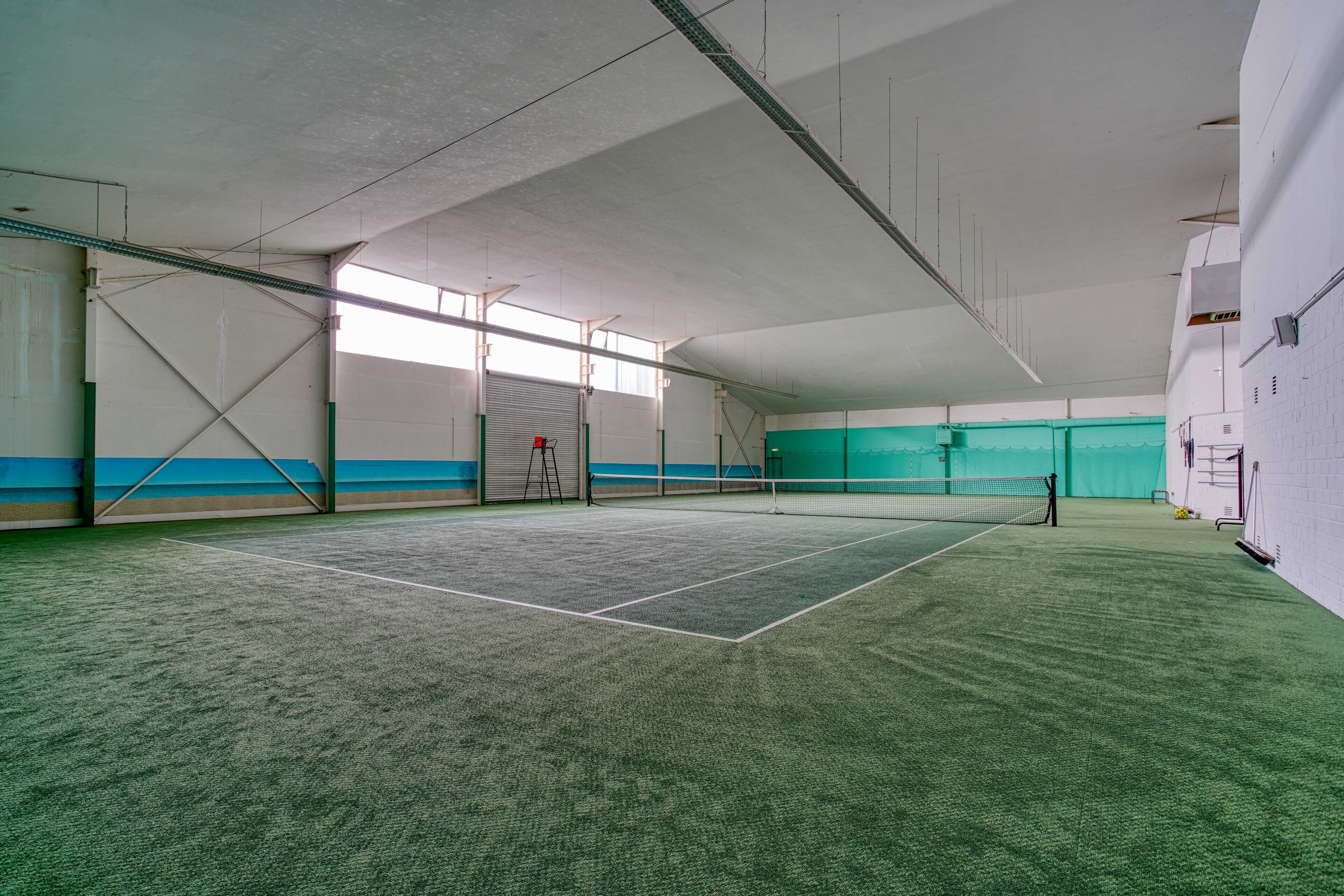 An indoor tennis court with a net, walls, and a door.
