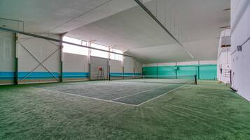 An indoor tennis court with a net, walls, and a door.