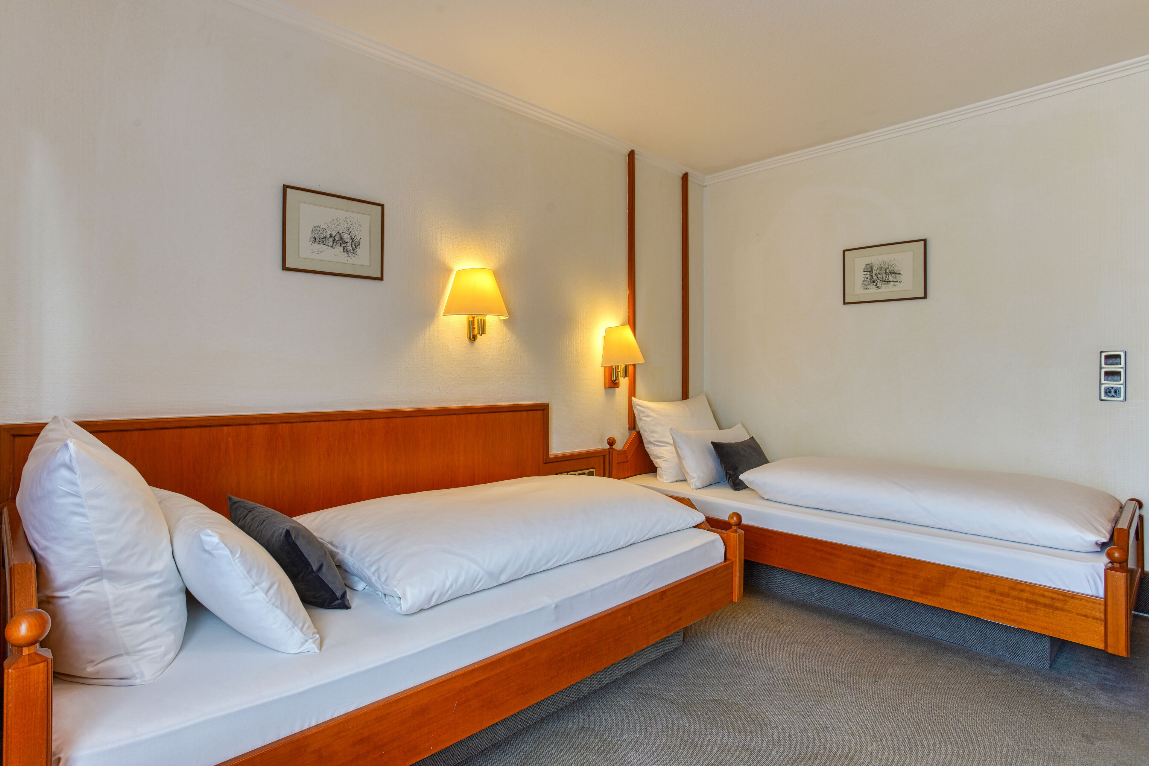 A hotel room with two wooden beds, a headboard, and two wall-mounted lamps.