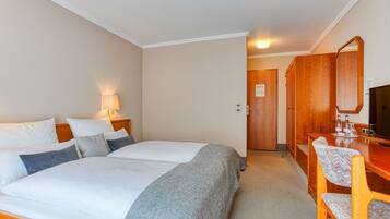 A hotel room with two beds, a desk, a chair, a lamp, and a television.