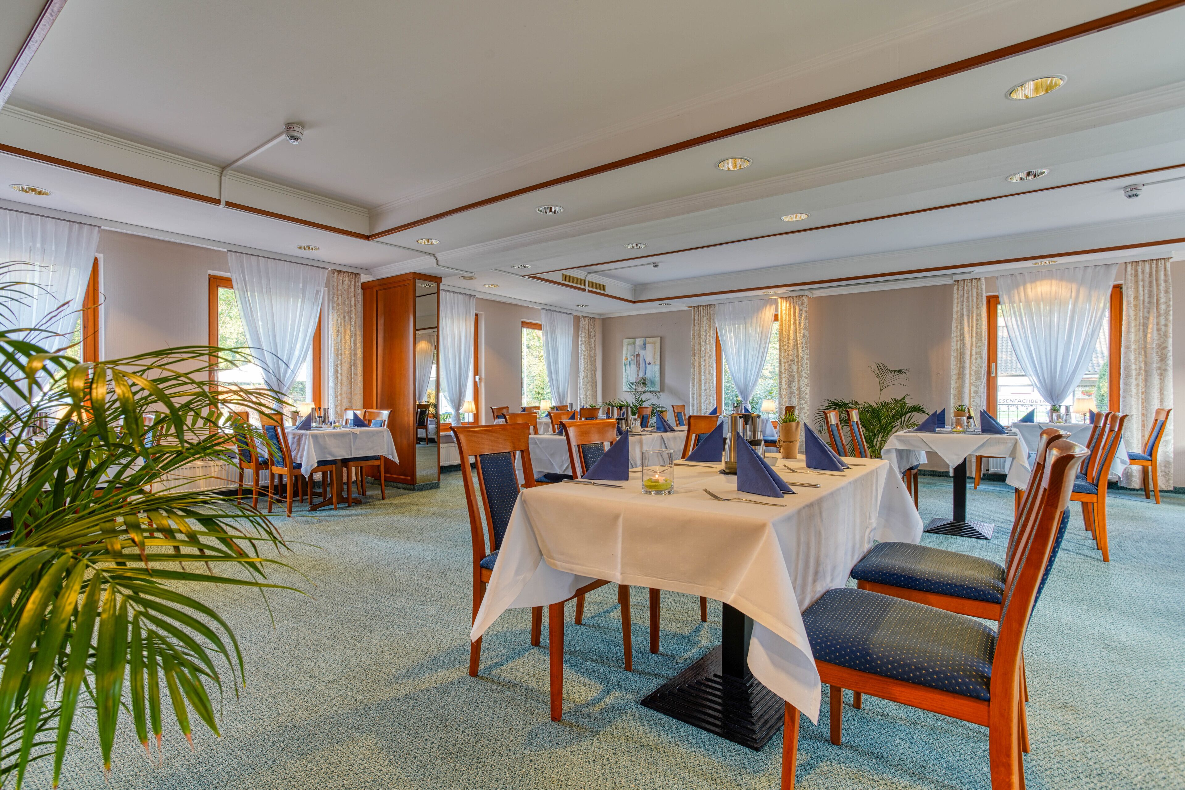 Un espace repas avec des tables disposées pour accueillir quatre personnes, des chaises en bois et un sol recouvert d’une moquette.