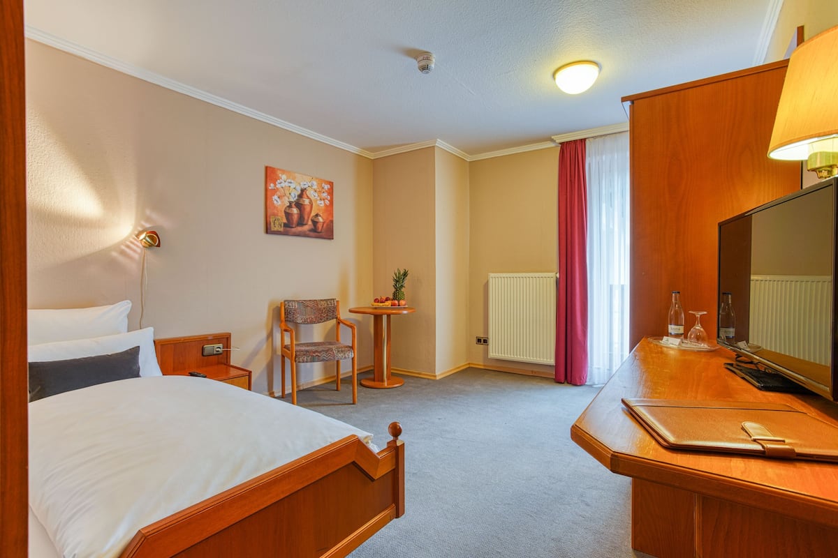 Ein Hotelzimmer mit einem Bett, einem Schreibtisch, einem Stuhl, einem kleinen Tisch mit Obst, einem Gemälde und einem Fernseher.