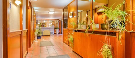 A hotel lobby with wooden paneling, a reception desk, and potted plants.