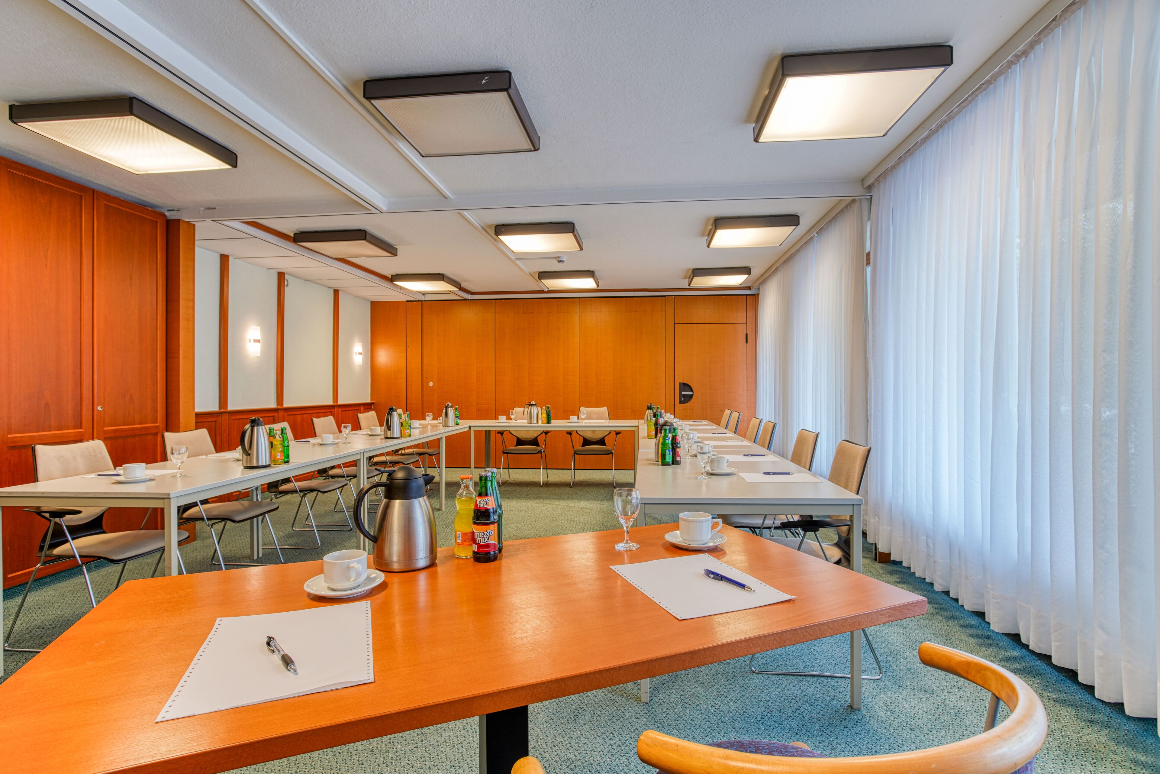 A conference room with multiple tables, chairs, and a long table with coffee and beverages.