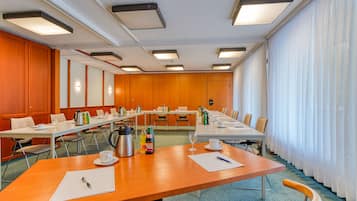 A conference room with multiple tables, chairs, and a long table with coffee and beverages.