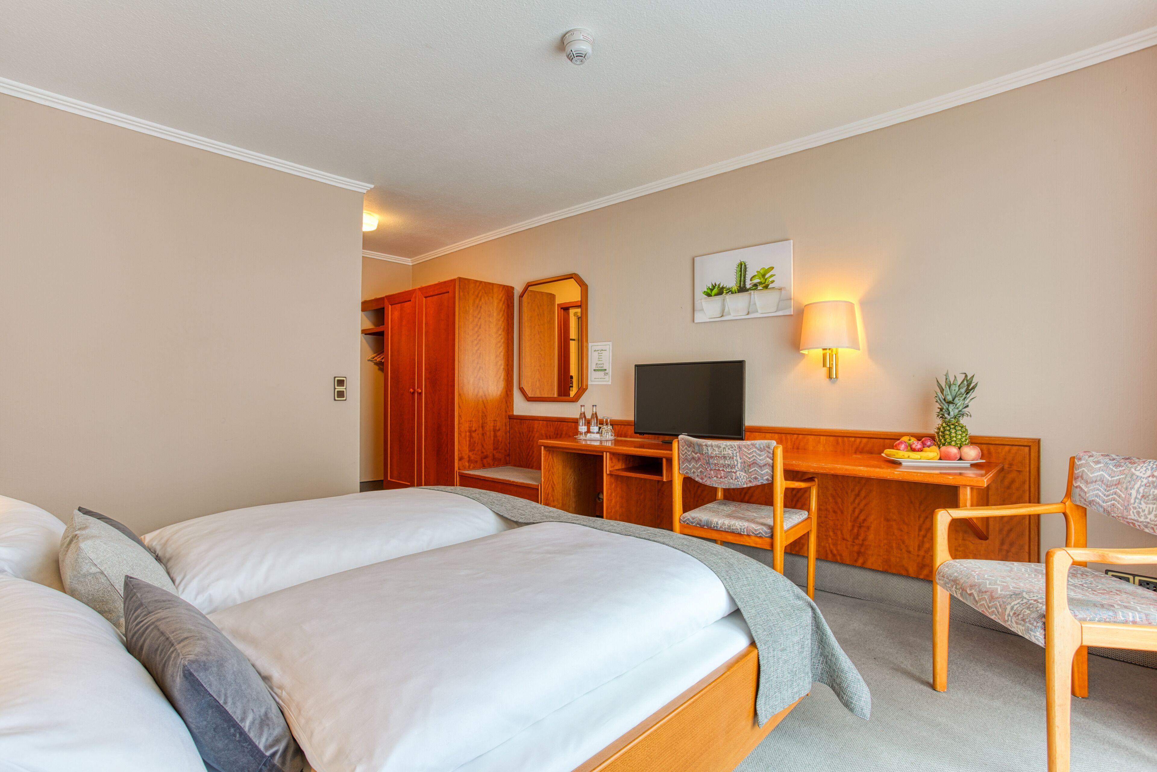 Habitación de hotel con dos camas, un escritorio con silla, televisión y una mesita con fruta.