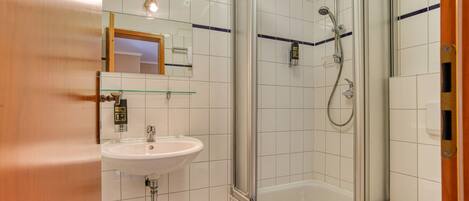 Un baño con ducha envuelta en vidrio, lavamanos e inodoro.