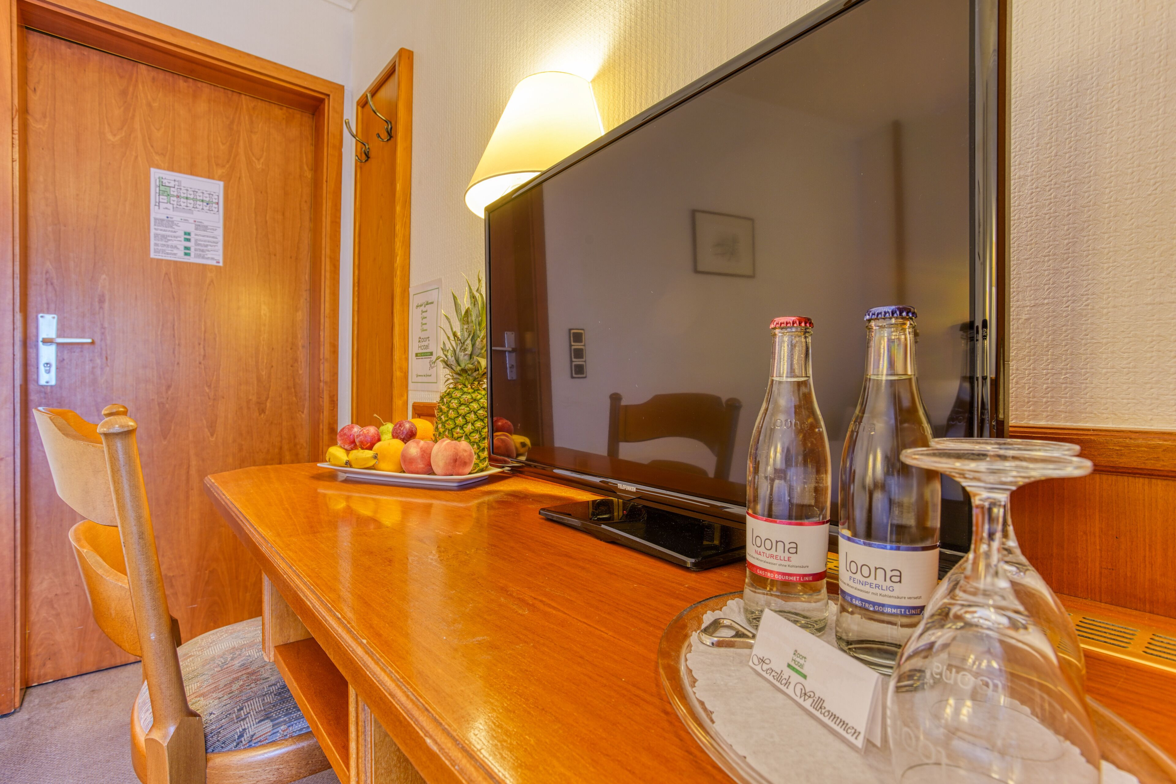A wooden table with a fruit tray, two bottles of Loona wine, and a glass on a tray.