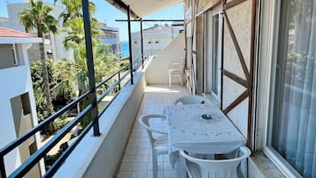 A covered balcony with a table and chairs, overlooking a residential area with palm trees and buildings.
