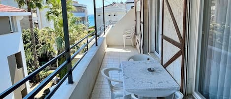 A covered balcony with a table and chairs, overlooking a residential area with palm trees and buildings.