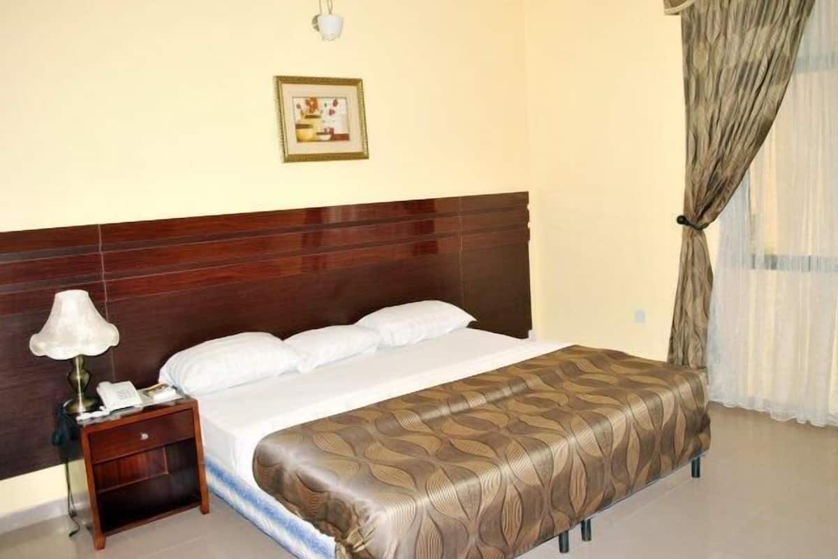 A hotel room with a wooden headboard, a bed with white linens, a bedside table with a lamp, and a framed picture on the wall.