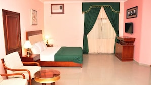 Une chambre d’hôtel comprenant un lit, deux chaises, une petite table, un téléviseur et un bureau avec une lampe.