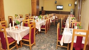 Un espace repas comprenant plusieurs tables et chaises, chaque table étant recouverte d’une nappe blanche et entourée de chaises rouges.
