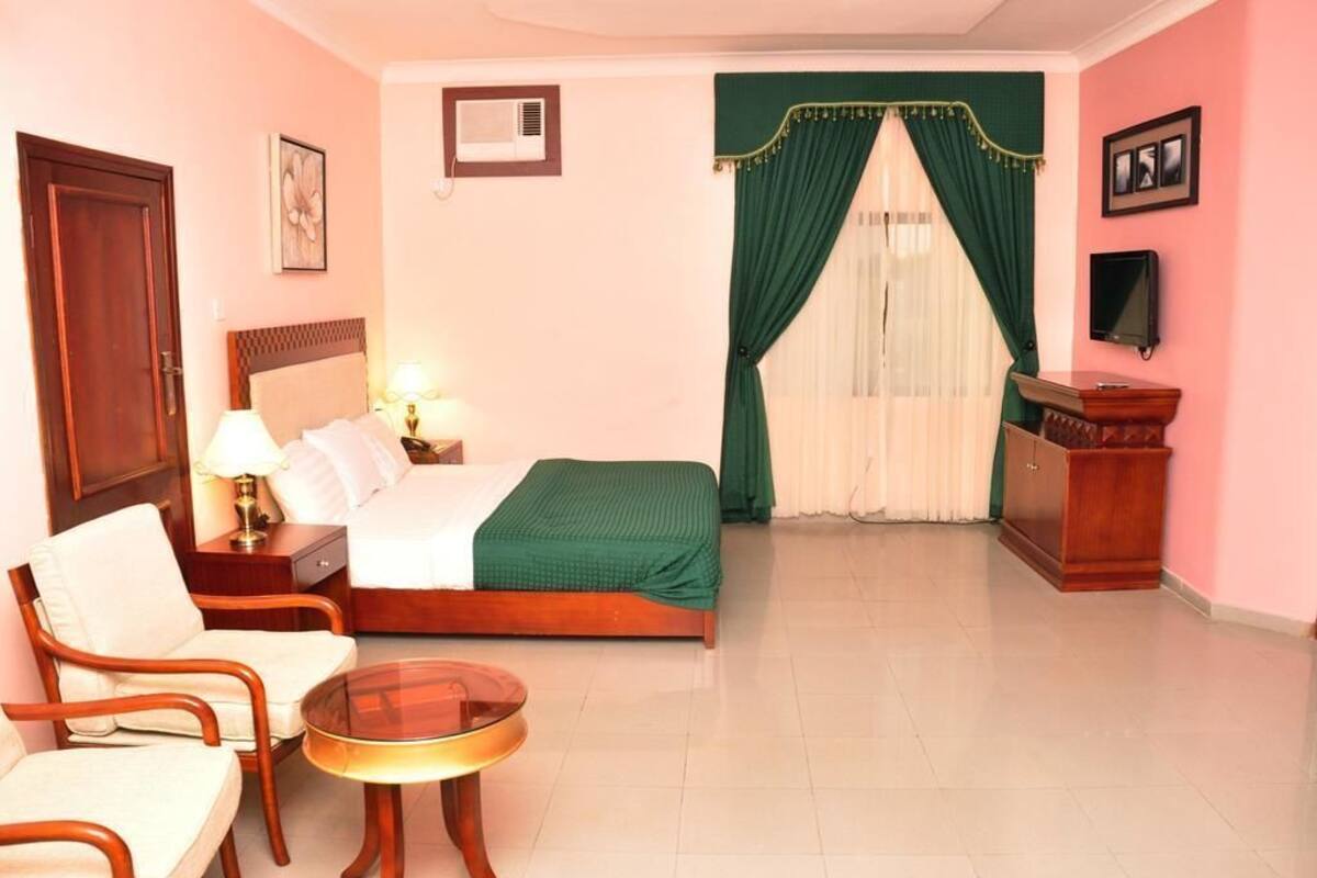 A hotel room with a bed, two chairs, a small table, a TV, and a desk with a lamp.