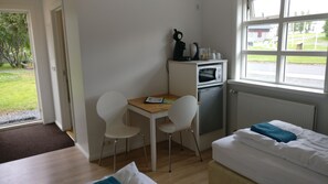 A small, well-lit room with a bed, a desk, two chairs, a microwave, and a radiator. - Birta Guesthouse (Egilsstaðir)