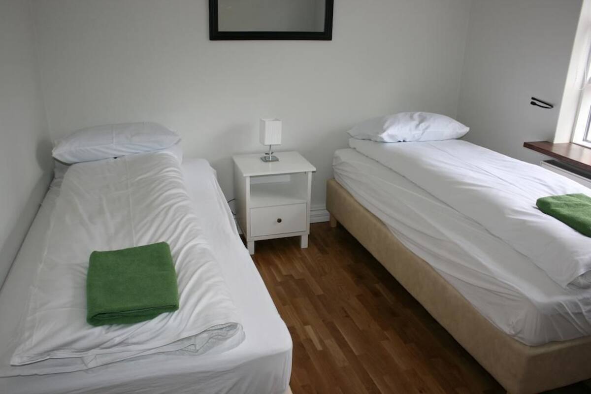 A room with two single beds, a small bedside table with a lamp, and a wooden floor.