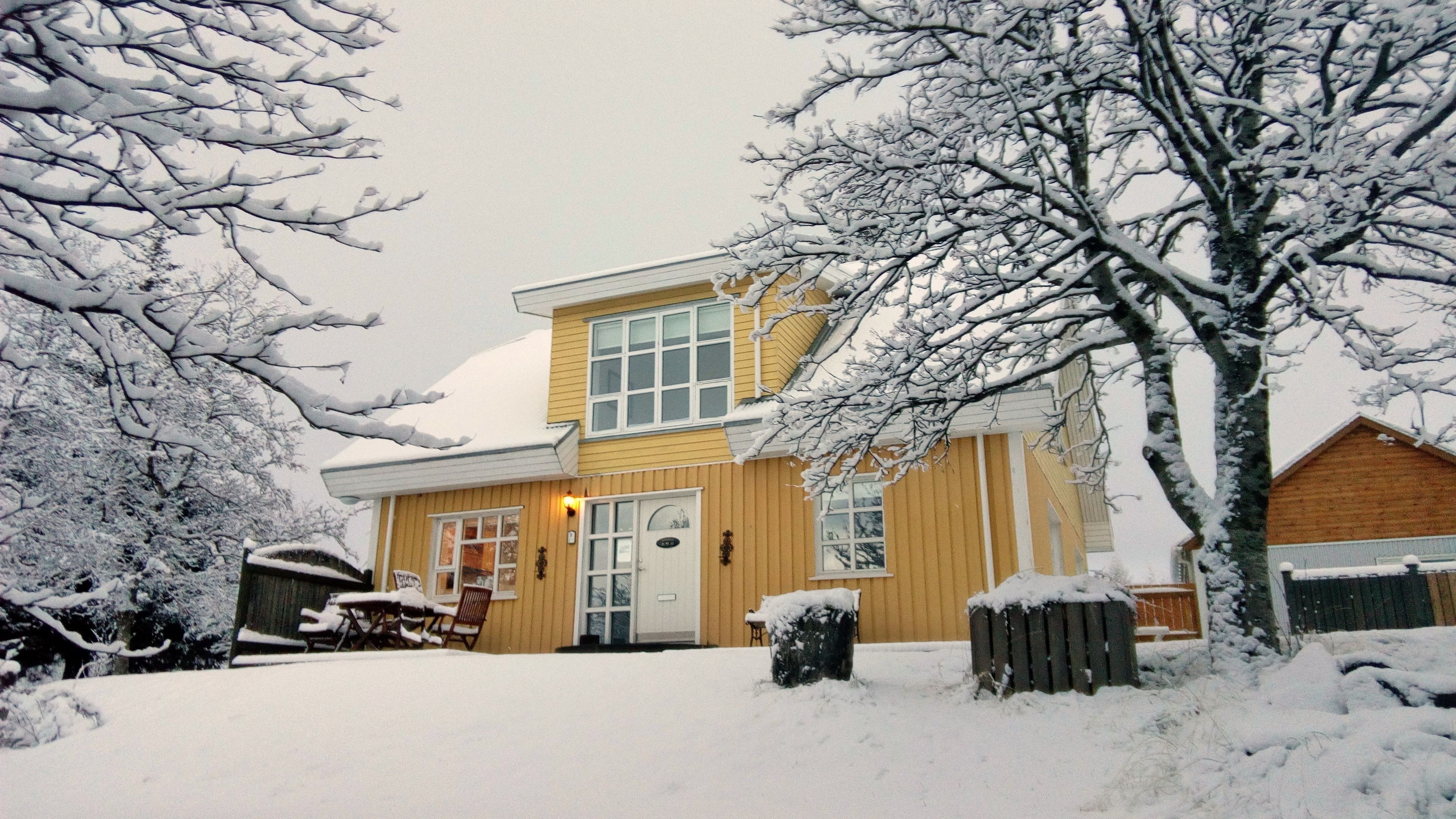 Ein zweistöckiges Haus mit verschneitem Vorgarten, einem Holzzaun und einer sichtbaren Haustür.