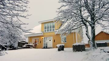 Ein zweistöckiges Haus mit verschneitem Vorgarten, einem Holzzaun und einer sichtbaren Haustür.