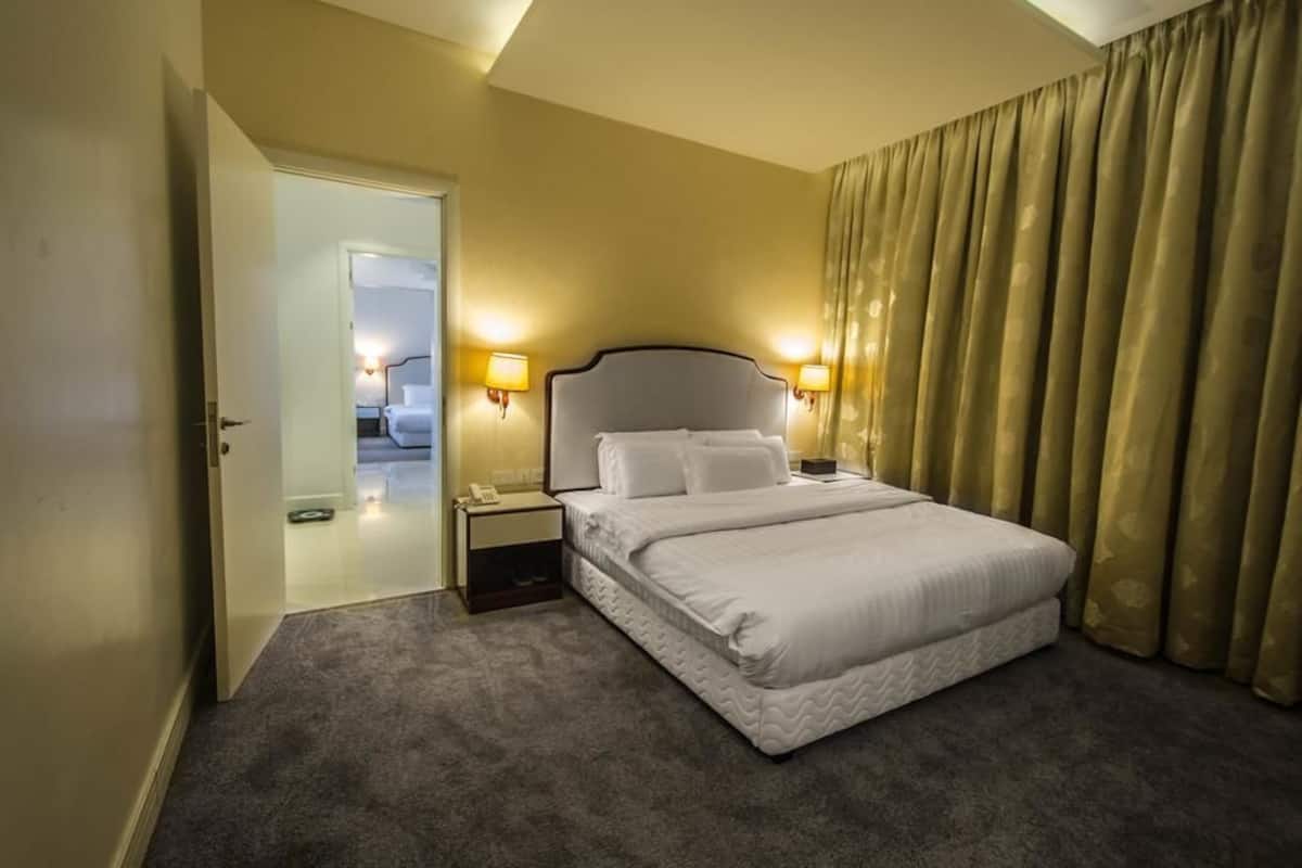 A hotel room with a bed, bedside lamps, a nightstand, and a door leading to another room.