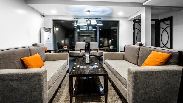 A modern living room with grey sofas, a black coffee table, and a glass partition separating the living area from the dining space. - Vanern Residence (Abuja)