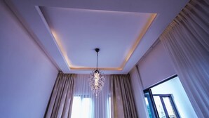 A room with a modern ceiling design, a chandelier, and large windows with curtains. - Vanern Residence (Abuja)