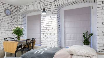 A room with white brick walls, a wooden table with chairs, a bed with pillows, and a hanging light fixture.