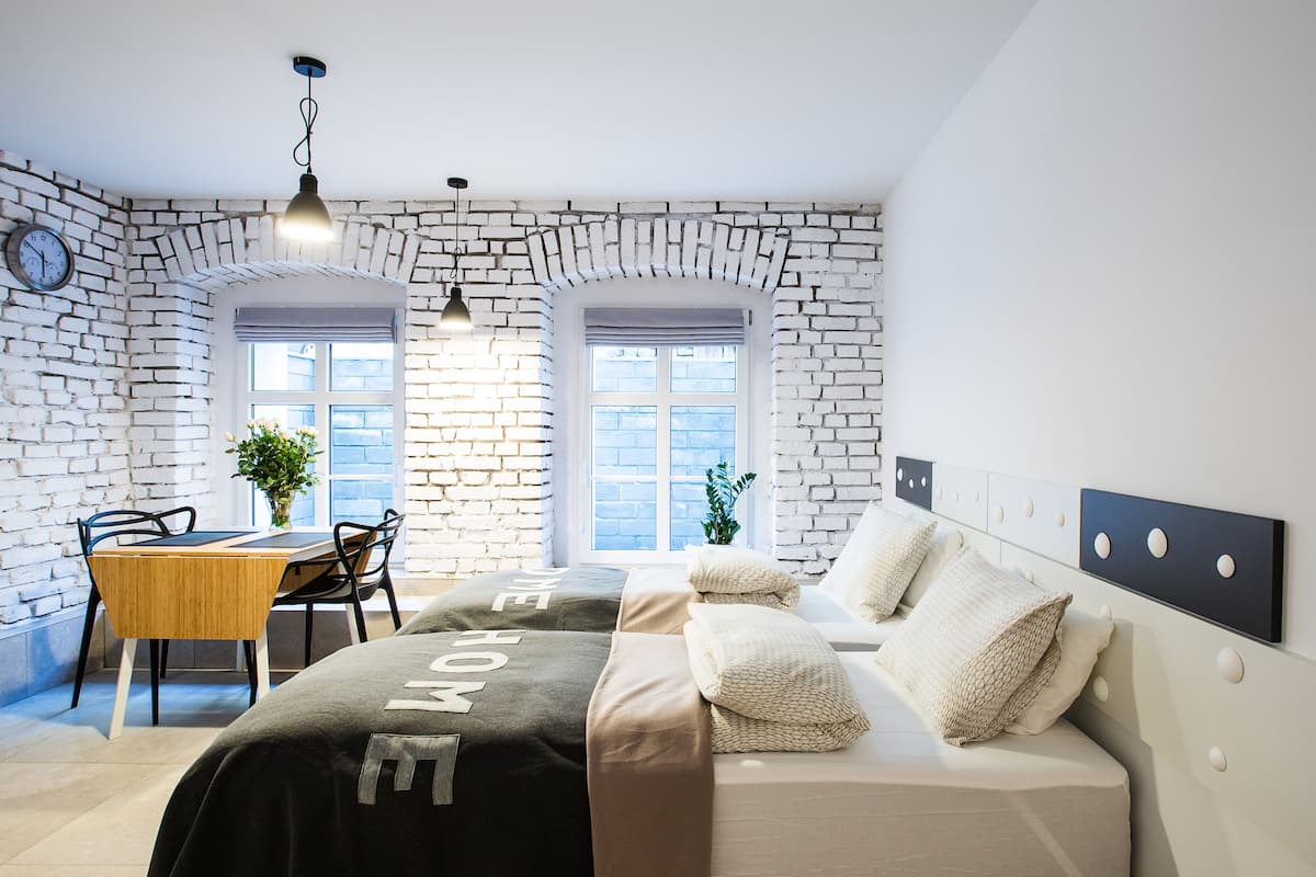 Ein Schlafzimmer mit Backsteinwand, einem Bett mit Kopfteil, einem Esstisch mit Stühlen und einem Fenster mit Blick.