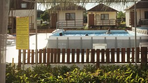 A swimming pool with a wooden fence in the foreground, surrounded by houses and a pergola overhead.