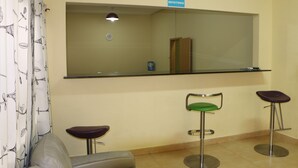 A reception area with a counter, two bar stools, a chair, and a sign indicating a waiting area. - SIS Hotel (Luanda)