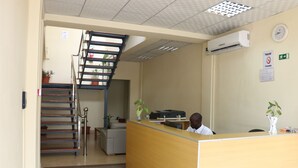 A reception area with a wooden desk, a staircase, and a clock on the wall. - SIS Hotel (Luanda)
