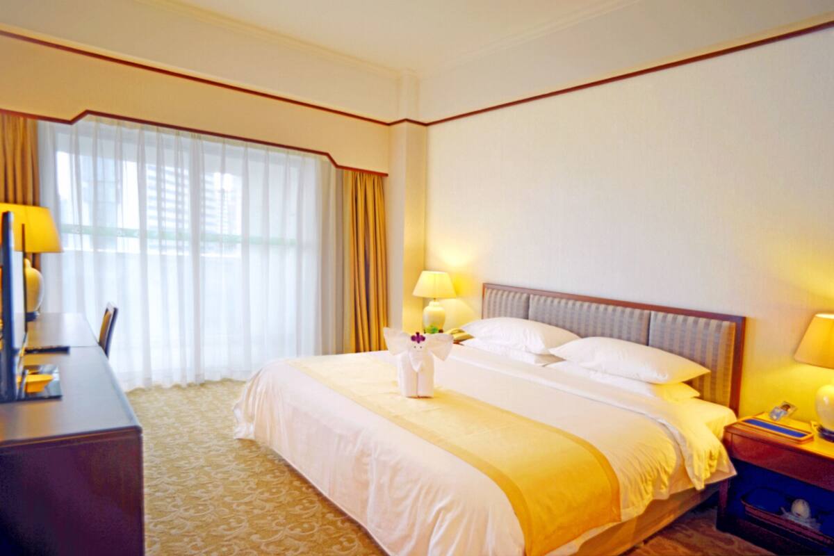 Une chambre d’hôtel avec un grand lit, deux lampes de chevet, un bureau avec une chaise et une fenêtre avec des rideaux.