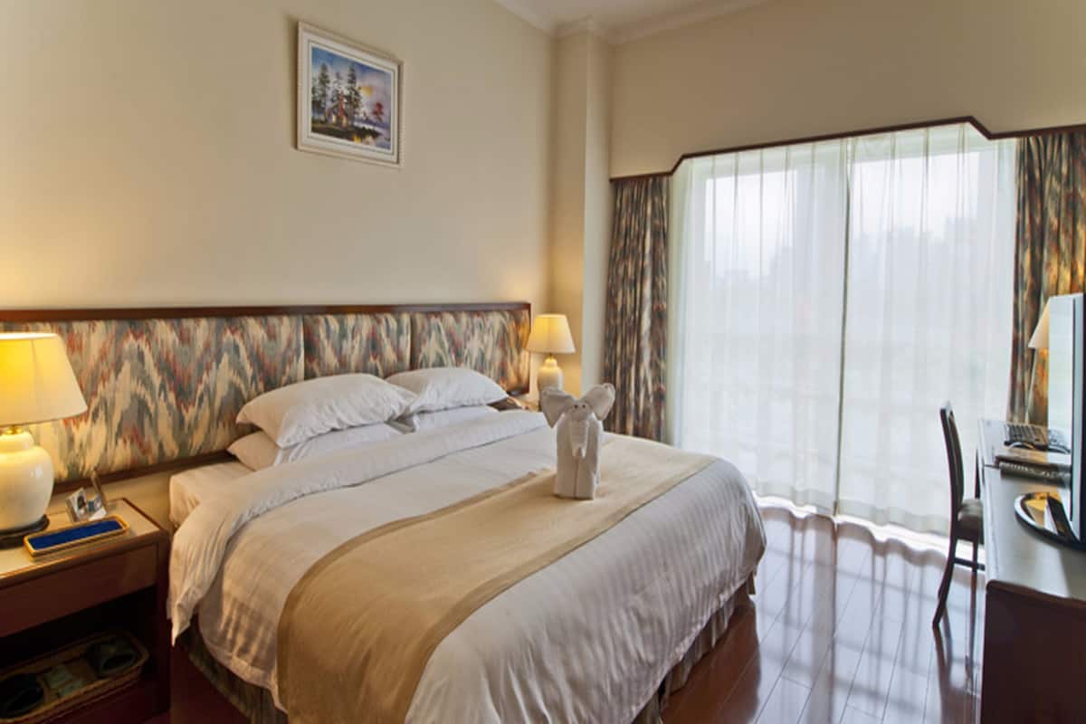 Une chambre d’hôtel avec un grand lit, deux lampes de chevet, un tableau encadré au mur et un bureau avec une chaise.