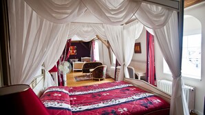 A bedroom with a canopy bed, a chair, a table, and a radiator. - Manoir François 1er (Vitry-le-Francois)