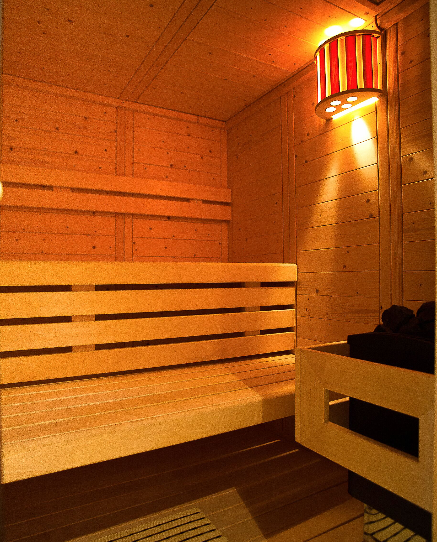Uma sauna de madeira com bancos e uma luminária fixada na parede.