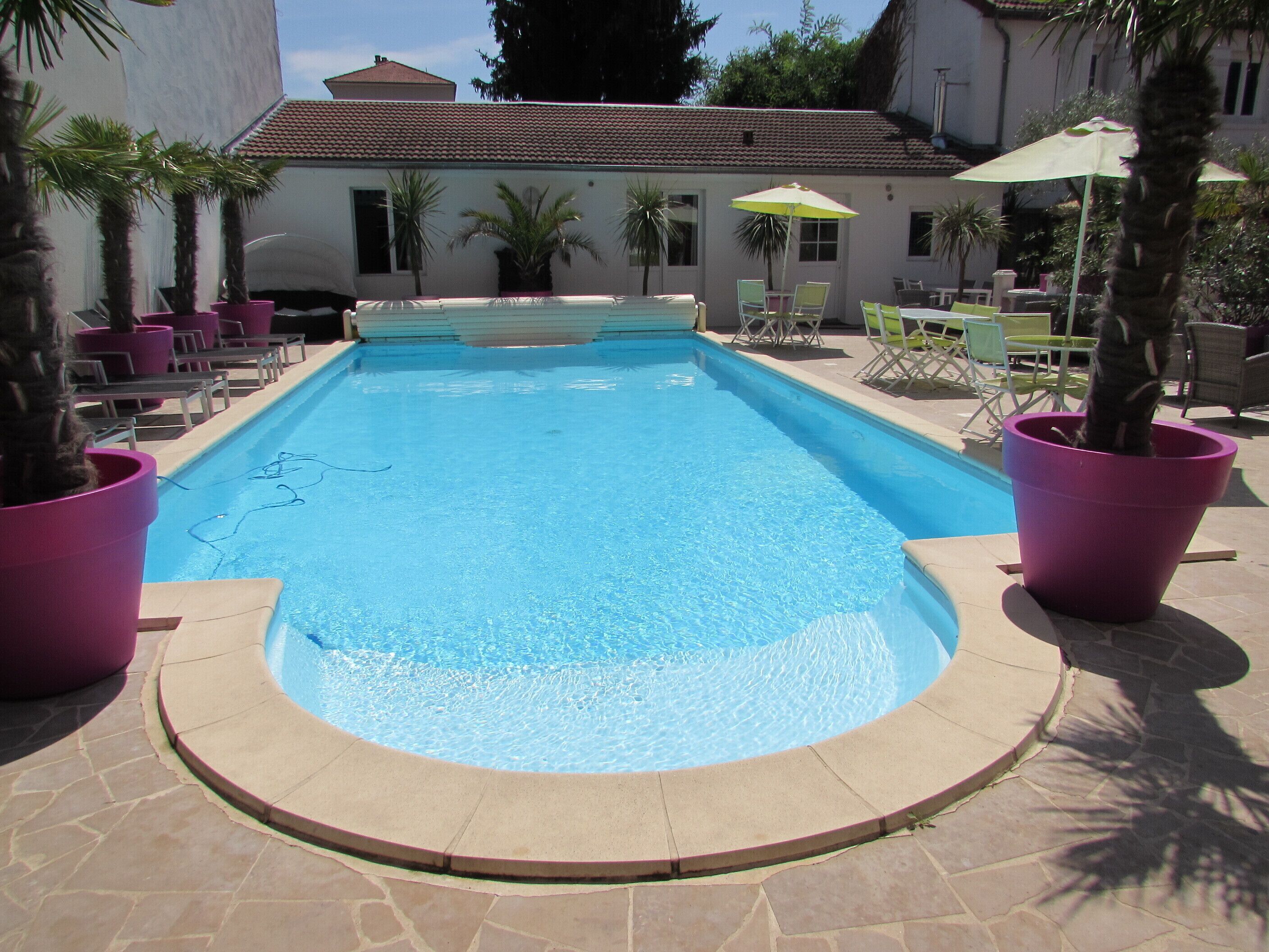 Una piscina con borde de baldosas, rodeada de plantas en macetas y mobiliario de exterior.