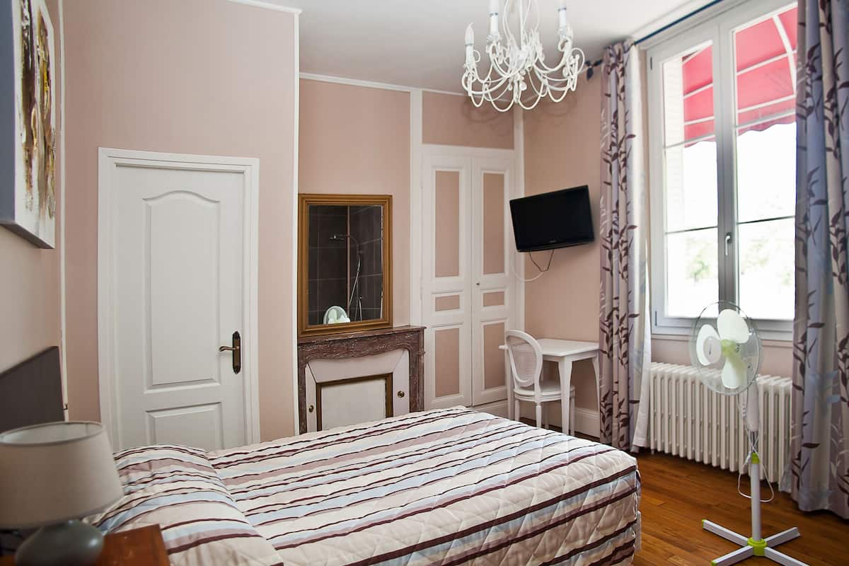 A bedroom with a bed, a desk, a chair, a TV, and a window with curtains.