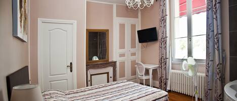 A bedroom with a bed, a desk, a chair, a TV, and a window with curtains.