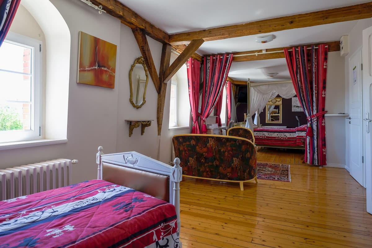 A bedroom with a wooden floor, a bed with a floral bedspread, a chair, and a large mirror.