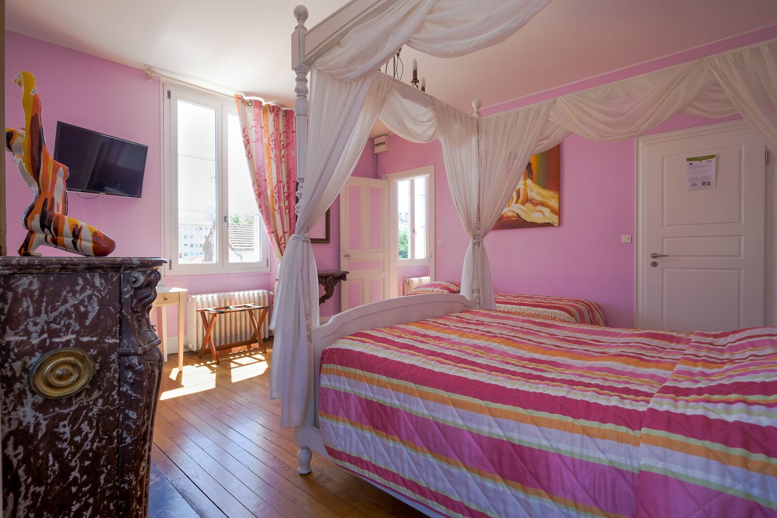 Une chambre à coucher avec un lit à baldaquin, une télévision, un radiateur et une fenêtre avec des rideaux.